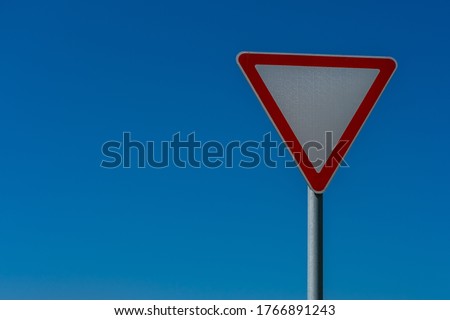 Triangular road sign (give way) close-up on a blue sky background.