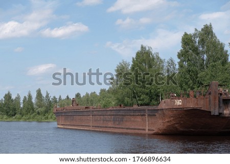 Large rusty barge anchored off the coast of a small river