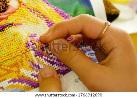 A woman embroiders a picture with beads. Needlework and home decoration concept