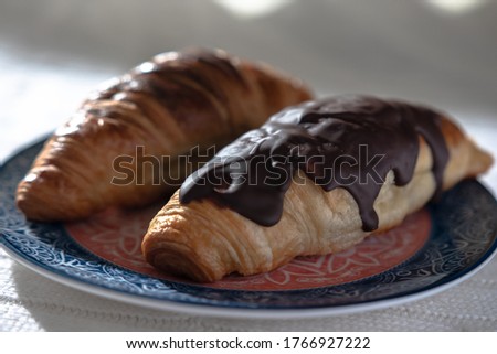 two croissants, with and without chocolate, and tea lie prepared for breakfast for tea or coffee in the early morning; bright sunlight from the window