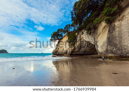 Woman takes pictures of magnificent landscape. Ocean tide in the Cathedral Cove. Mirror reflections of clouds in wet sand. Travel to New Zealand. The concept of exotic, ecological and photo tourism