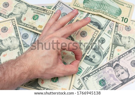 Man shows sign okay with fingers, dollar bills in the background, male hand, close-up