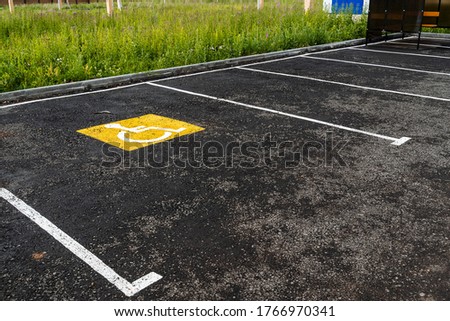 a yellow sign on the asphalt shows a Parking place for people with disabilities, a road sign, markings on the road