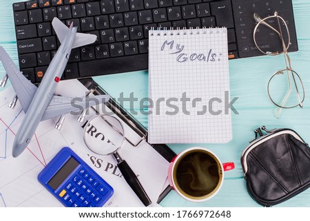 2018 goals on notebook with traveler accessories glasses wallet and airplane on wooden table top background. Flat lay travel concept.