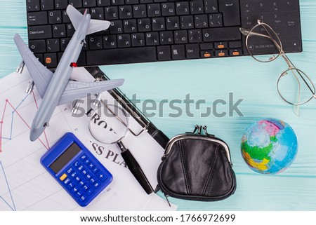 A lot of messy stuff on the blue table with keyboard. Toy airplane globe wallet glasses. Concept of planning flight.