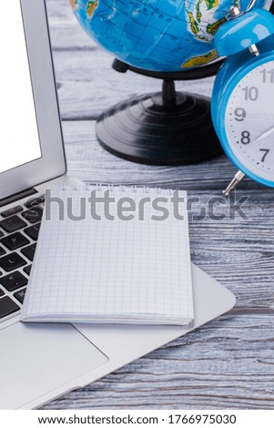 Close up blank notepad on a laptop pc. Time and globalization concept. Earth globe and alarm clock on white wooden table.