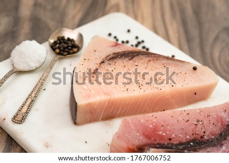 Raw swordfish. Two pieces of fresh raw fish steaks with salt and black pepper close up on marble cutting board on wooden kitchen table Royalty-Free Stock Photo #1767006752