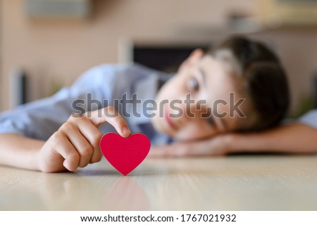 A girl lies on a table and holds a pink heart with her finger. Focus on the heart, blurred background