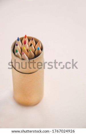 Close up picture of colorful pencils in the round box in light background, as school concept. Colourful pencils for drawing in tube box with copy space for text on right side. Stationery picture.