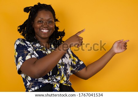 Advertisement concept. Positive, pretty, caucasion woman with beaming smile in jeans shirt on grey background is pointing with her two index finger and looking on empty copy space.