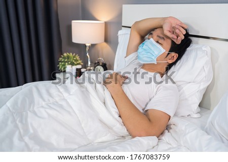 sick man in medical mask is headache and suffering from virus disease and fever in bed, coronavirus (covid-19) pandemic concept. Royalty-Free Stock Photo #1767083759