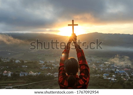 Human praying to the GOD while holding a crucifix symbol with bright sunbeam on the sky
