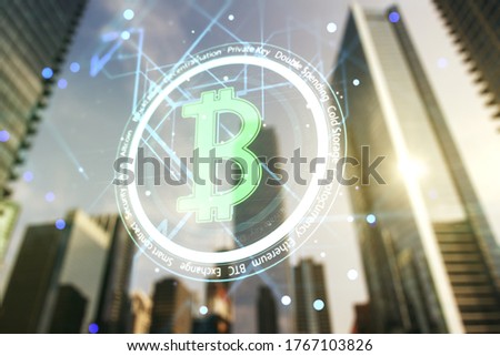 Double exposure of creative Bitcoin symbol hologram on modern skyscrapers background. Cryptocurrency concept