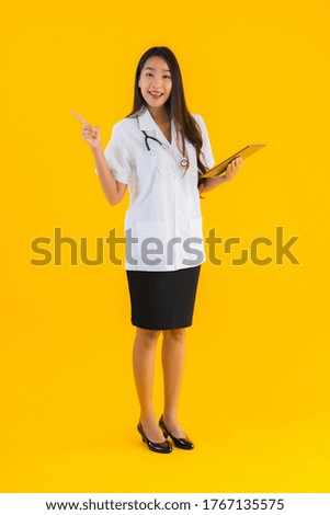 Portrait beautiful young asian doctor woman use smart tablet device on yellow isolated background