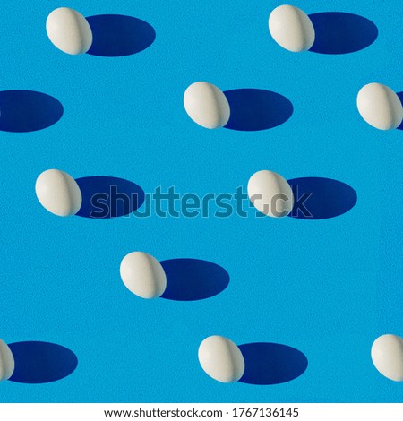 Creative geometric seamless pattern in pop art style. Repeating white eggs on a blue background. View from above. Flat lay.