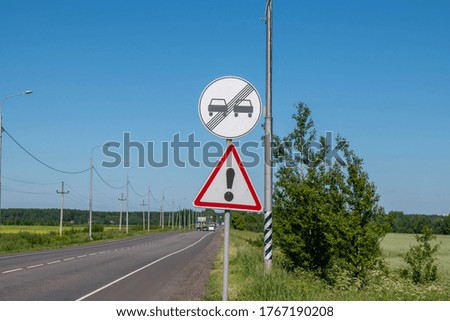 Old warning road signs on a country road against the blue sky and cars driving in the background