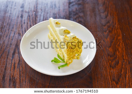 Sweet pistachio dessert with vanilla cream and nuts on white plate. Slice of pistachio cake. Tea time. Served over dark rustic wooden background.