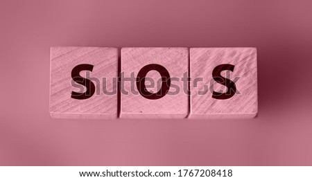 SOS symbol on wooden cubes, toned in dusty rose pink. Save Our Souls call for help concept.