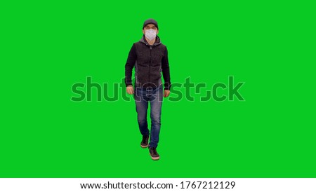 Man in protective mask and casual clothing walking during pandemic COVID-19 against green screen background, Chroma key