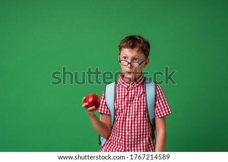 funny, surprised schoolboy holds an Apple in his hand, standing against the blackboard. an inquisitive child is happy to return to school. Isolated Studio shot on a green background. Back to school.