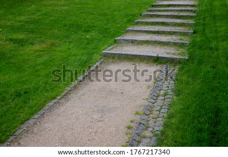park stairs made of beige gravel material bordered by granite cubes follow the gravel path with a longitudinal groove of granite stone cubes around the lawn gutter channel