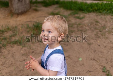 A little boy of two years in a blue jumpsuit and a white T-shirt walks in the park and is surprised by everything that is happening around him. High quality photo