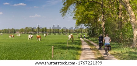 Panorama of a couple riding their bicycle at a dirt road in Overijssel, Netherlands Royalty-Free Stock Photo #1767221399