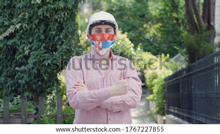 Virus and disease prevention concept. Portrait of a male worker wearing a protective medical mask with an Serbia flag. Protection against coronavirus and other diseases.