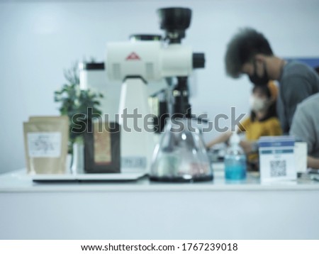 The Picture of 
blur barista in apron and face mask standing behind counter bar ready to give Coffee Service at the modern coffee shop, Modern cafe business, Social distancing concept.