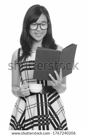 Young happy Asian businesswoman reading book while holding coffee cup
