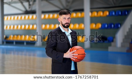 A young man with beard in a blazer in game basketball court. Sportsman standing with ball in hands