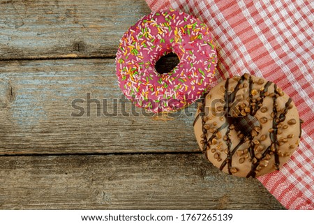 A pink and chocolate doughnut on a wooden planks background with a napkin on a vintage wood background with copy space.