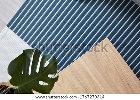 Wooden table in scandinavian colors and blue navi carpet in gray stripe. Defocused leaf of monstera.