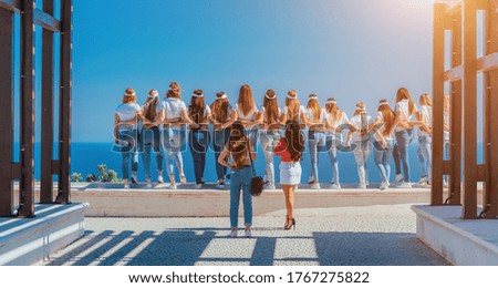 successful team of girls in white t-shirts and blue jeans take photos hugging each other on the sea background. Friendship, Teamwork, Harmony and Help Concept.