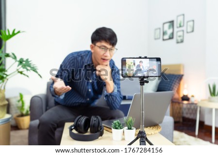 Asian man online influencer recording video live streaming, using digital smartphone camera present product review for theme about video blogging focus on camera screen show on social media