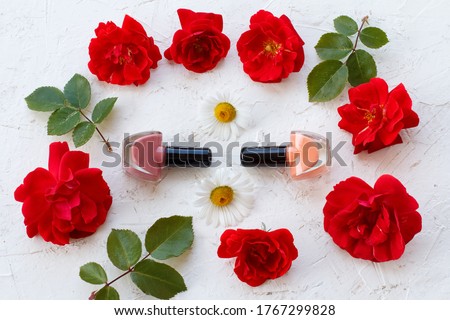 Bottles with nail polish on a white background with buds of rose flowers. Woman cosmetics and accessories. Top view.