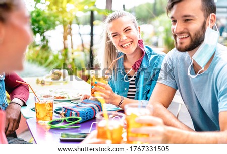Friends drinking at cocktail bar with opened face masks - New normal friendship concept with people having fun together toasting drinks at fashion dinner - Bright vivid filter with focus on woman Royalty-Free Stock Photo #1767331505