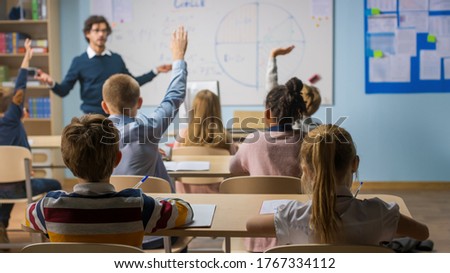 Caring Teacher Explains Lesson to a Classroom Full of Diverse Children. In School with Group of Smart Multiethnic Kids Learning Science, Whole Classroom Raising Hands Knowing Answer. Royalty-Free Stock Photo #1767334112