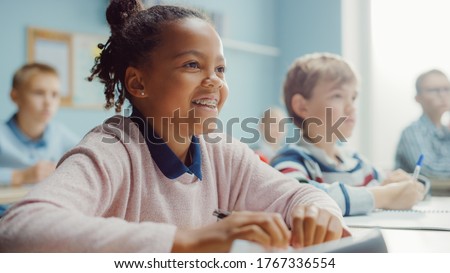 In Elementary School Class: Portrait of a Brilliant Black Girl with Braces Smiles, Writes in Exercise Notebook. Junior Classroom with Diverse Group of Children Learning New Stuff Royalty-Free Stock Photo #1767336554