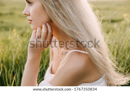 Portrait of a young woman with long blonde hair, in soft sun light, backlit, sitting in a field. Royalty-Free Stock Photo #1767350834