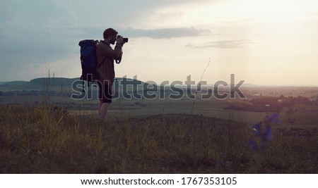 Backpacker taking landscape photos using dslr camera standing on hill, active lifestyle concept