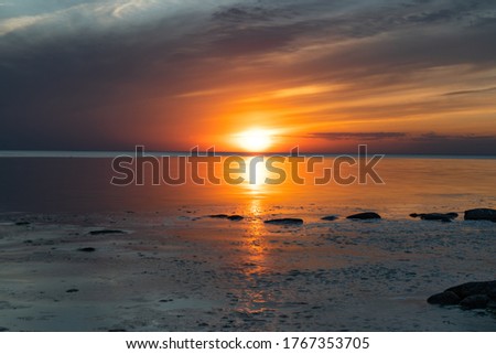 Amazing sunset on the Kabli Beach in Estonia. Darker looking image. Calm water during sunset last's moments. Beach full of stones and bushes. Golden hour ending, blue hour starting