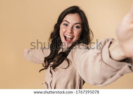 Image of cheerful cute woman laughing and taking selfie photo isolated over beige background