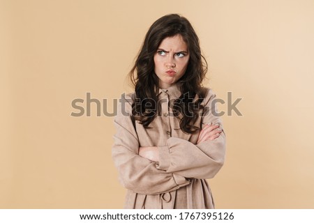 Image of resentful brunette woman posing and looking aside isolated over beige background Royalty-Free Stock Photo #1767395126