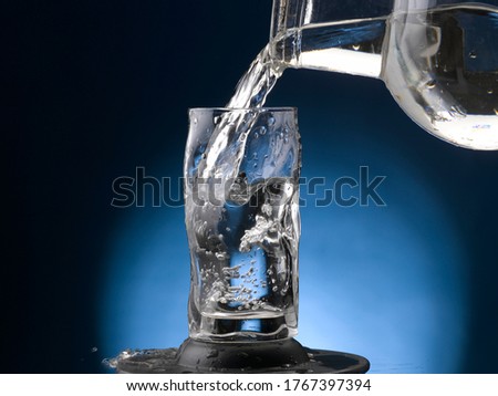 water pouring into highball glass making bubbles. close-up. spotlight on blue background