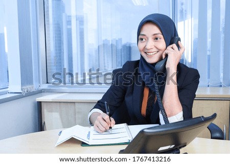 A young Asian woman answering the telephone in the office 