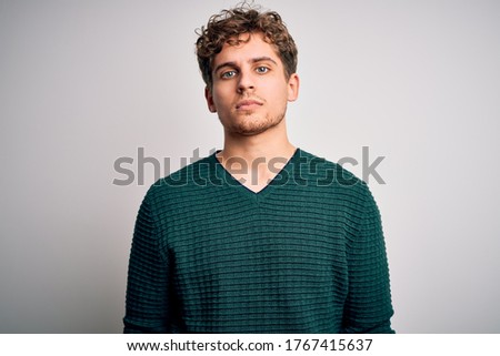 Young blond handsome man with curly hair wearing green sweater over white background Relaxed with serious expression on face. Simple and natural looking at the camera. Royalty-Free Stock Photo #1767415637
