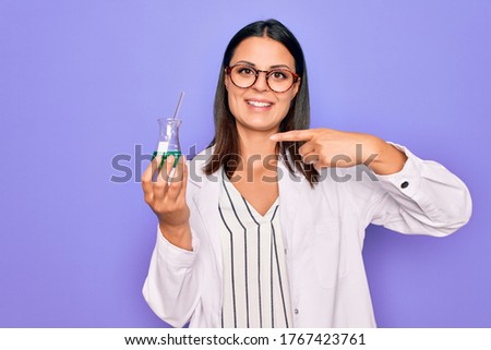Young beautiful brunette scientist woman wearing coat and glasses holding test tube Smiling happy pointing with hand and finger