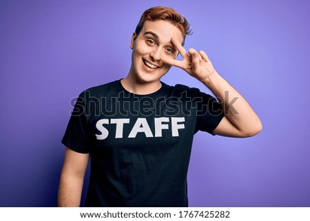 Young handsome redhead worker man wearing staff t-shirt uniform over purple background Doing peace symbol with fingers over face, smiling cheerful showing victory