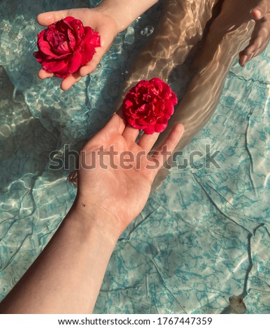 Mom and baby are sitting in the pool with clear water and are holding red beautiful roses in their hands